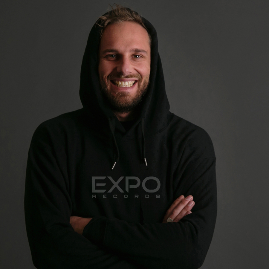 Der Künstler Dynamic Range lächelt mit verschränkten Armen in die Kamera. Er trägt einen schwarzen Kapuzenpullover.