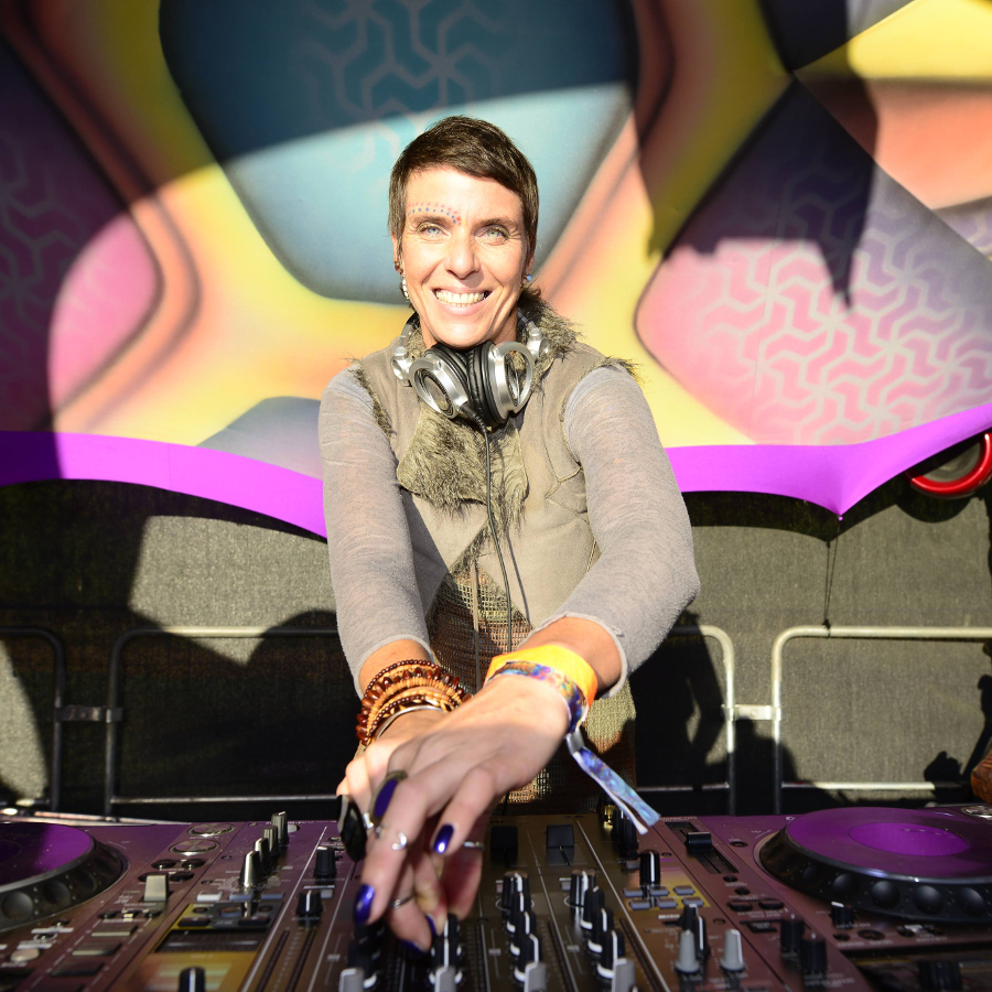 Djane Melburn an den Turntables. Sie lächelt in die Kamera.