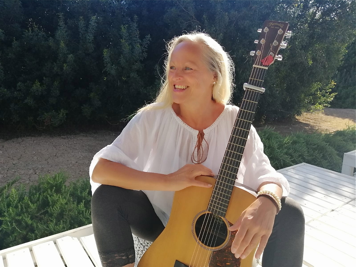 Shoshanna Die Künstlerin sitzt mit der Gitarre vor ihr auf der Terasse. Sie schaut nach links.