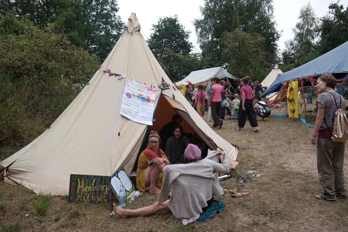 Healing Sitter Tipi des Healing Sitting Programms auf dem New Healing Festival. Vor dem Tipi sitzen drei Frauen
