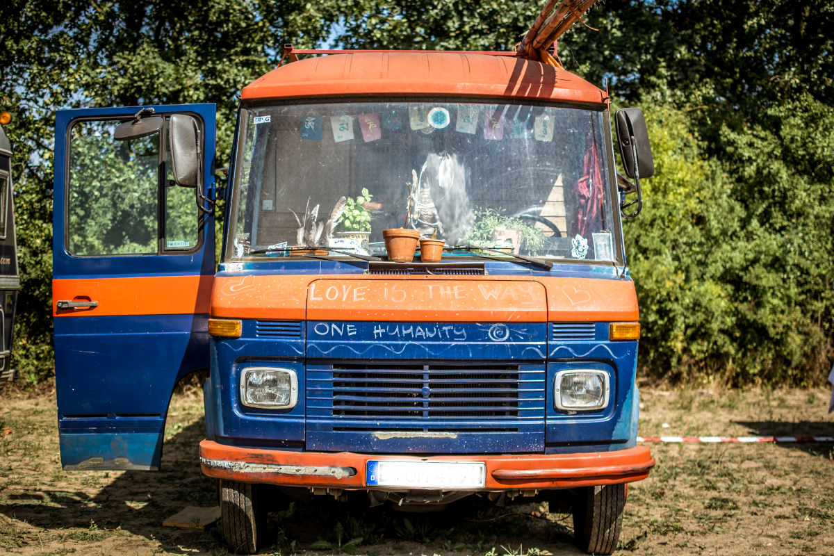 Hippiebus Frontale Ansicht eines alten Minibusses in blau und orange. Die linke Tür steht offen.
