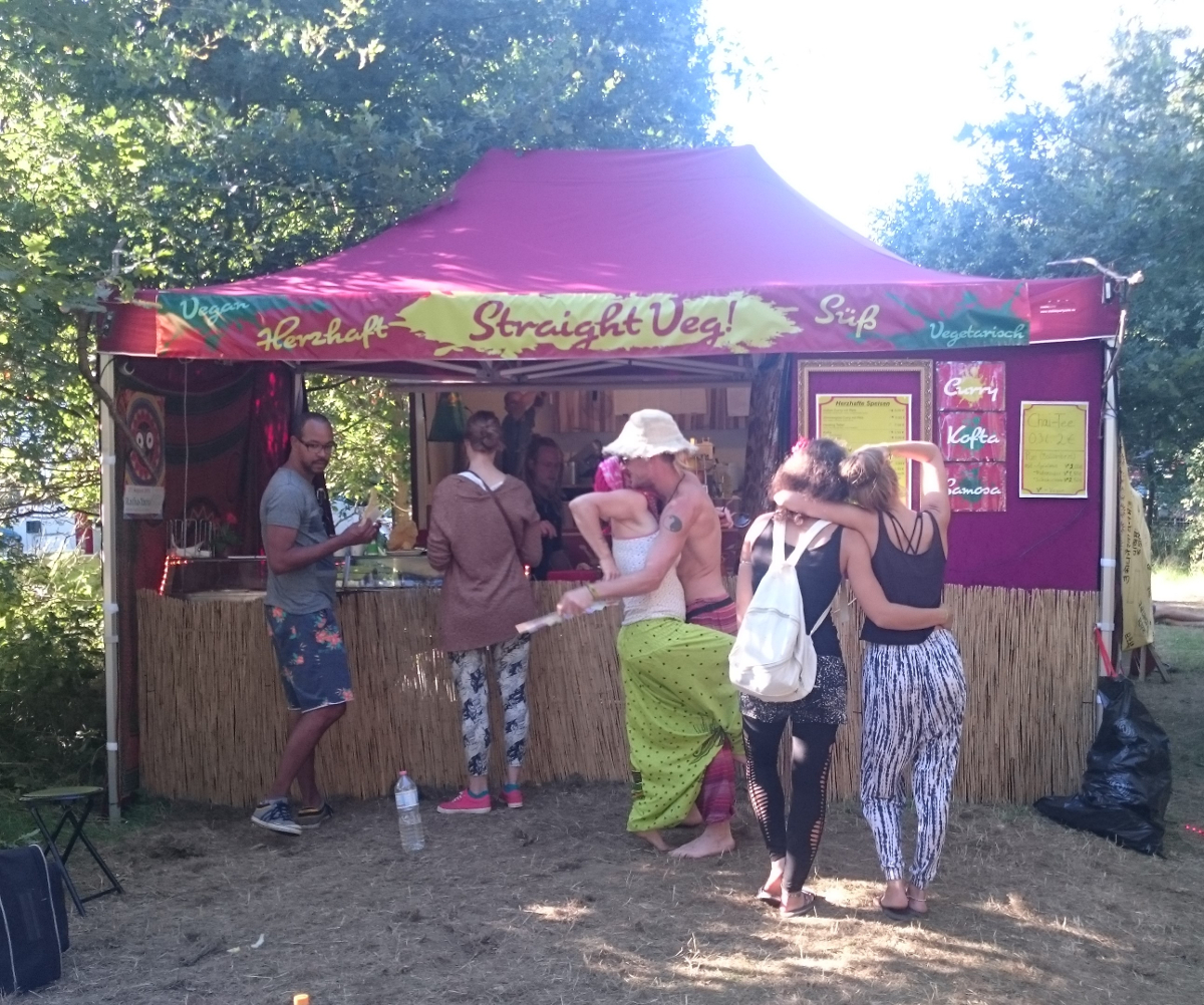 Prasad Ein Stand an dem vegane und ayurvedische Gerichte verkauft werden. Davor stehen einige Menschen, die etwas bestellen oder essen.